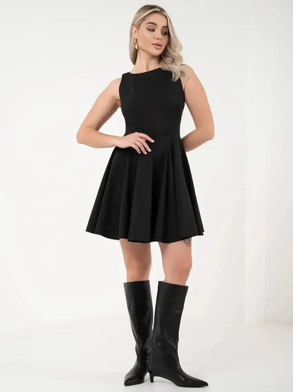 A model wearing a sleeveless black dress with a flared skirt, paired with knee-high black boots.