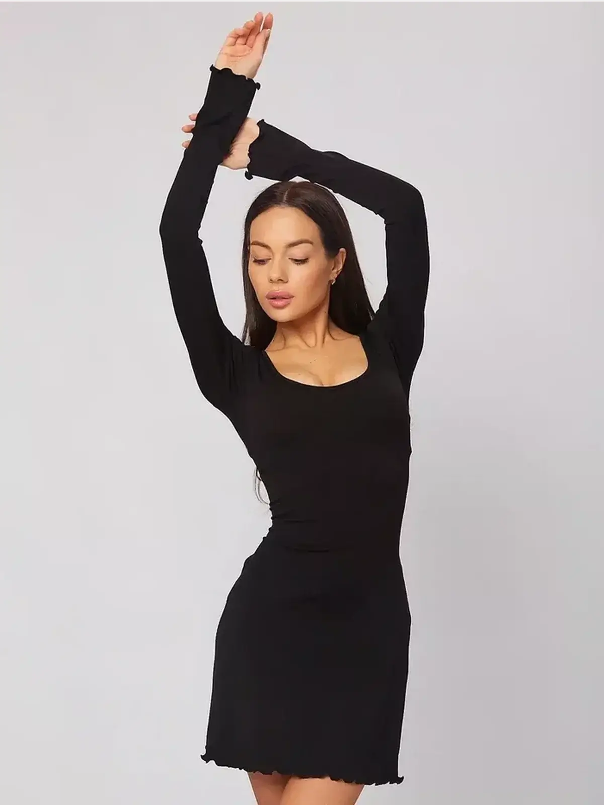 Model wearing a black mini dress with long sleeves and a U-shaped neckline, showcasing a stylish silhouette.
