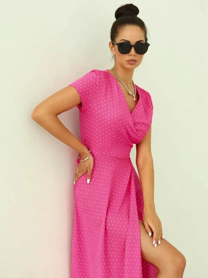 Woman in a vibrant pink polka dot Blush Radiance Maxi Dress, featuring a V-neckline and leg-baring slit.