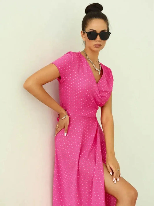 Woman in a vibrant pink polka dot Blush Radiance Maxi Dress, featuring a V-neckline and leg-baring slit.