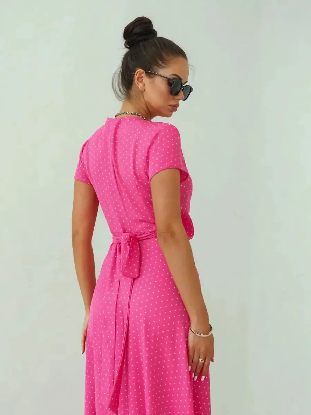 Woman in a pink polka dot maxi dress with short sleeves and a bow, showcasing a playful and feminine style.