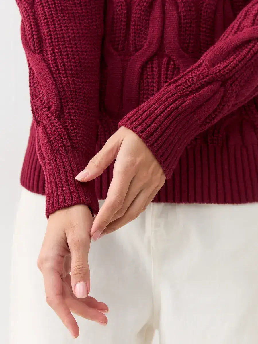 Close-up of hands adjusting sleeves of Bordeaux Knitwear by Lauven, showcasing the rich cable-knit design.
