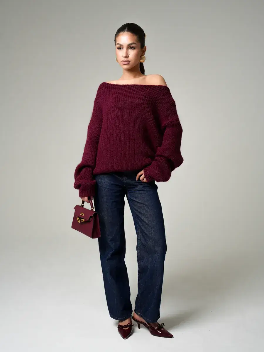 Model wearing Bordeaux Sweater by Lauven, oversized off-shoulder knit in deep wine paired with jeans.