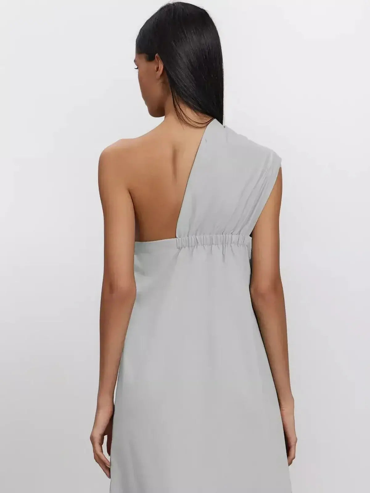 Back view of the Cascade Maxi Dress in breathable cotton, showcasing its elegant one-shoulder design and elasticated back.