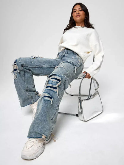 Woman wearing Celeste Pullover by Lauven with distressed jeans, seated on a clear chair, styled for casual elegance.