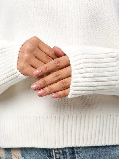 Close-up of hands wearing the Celeste Pullover by Lauven, showcasing its soft ivory fabric and ribbed cuffs.