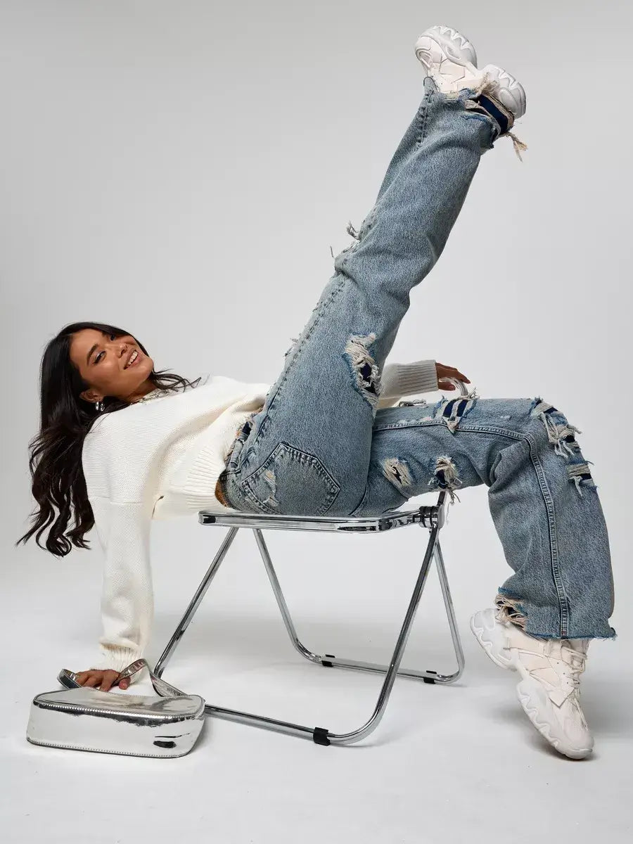 Woman wearing Celeste Pullover with ripped jeans, posing playfully on a chair, showcasing Lauven brand style.