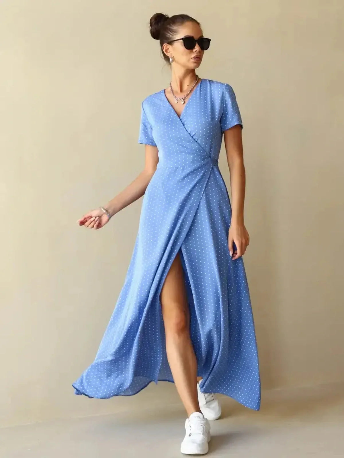 Model wearing the Celeste Wrap Maxi Dress in soft blue polka dots, showcasing a flattering V-neckline and thigh-high slit.