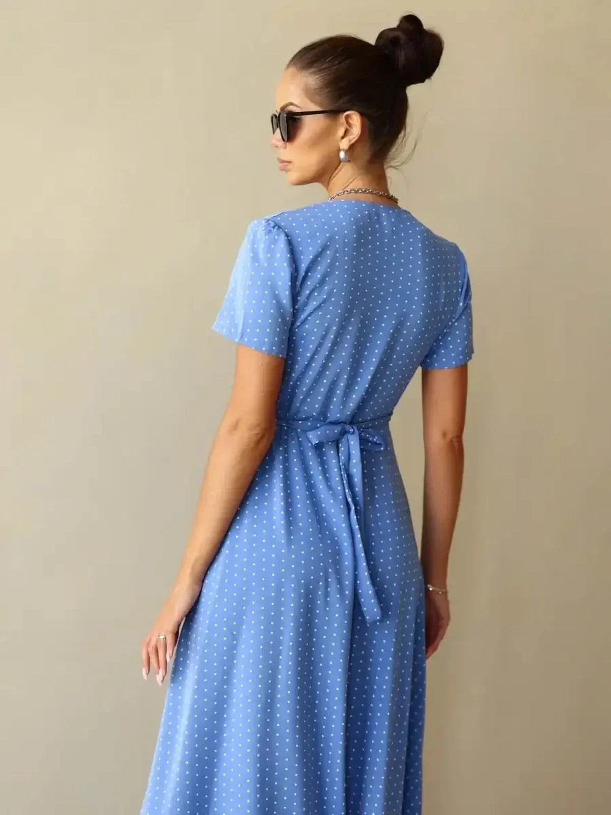 Back view of the Celeste Wrap Maxi Dress in soft blue polka dots, featuring a tied waist and modern silhouette.