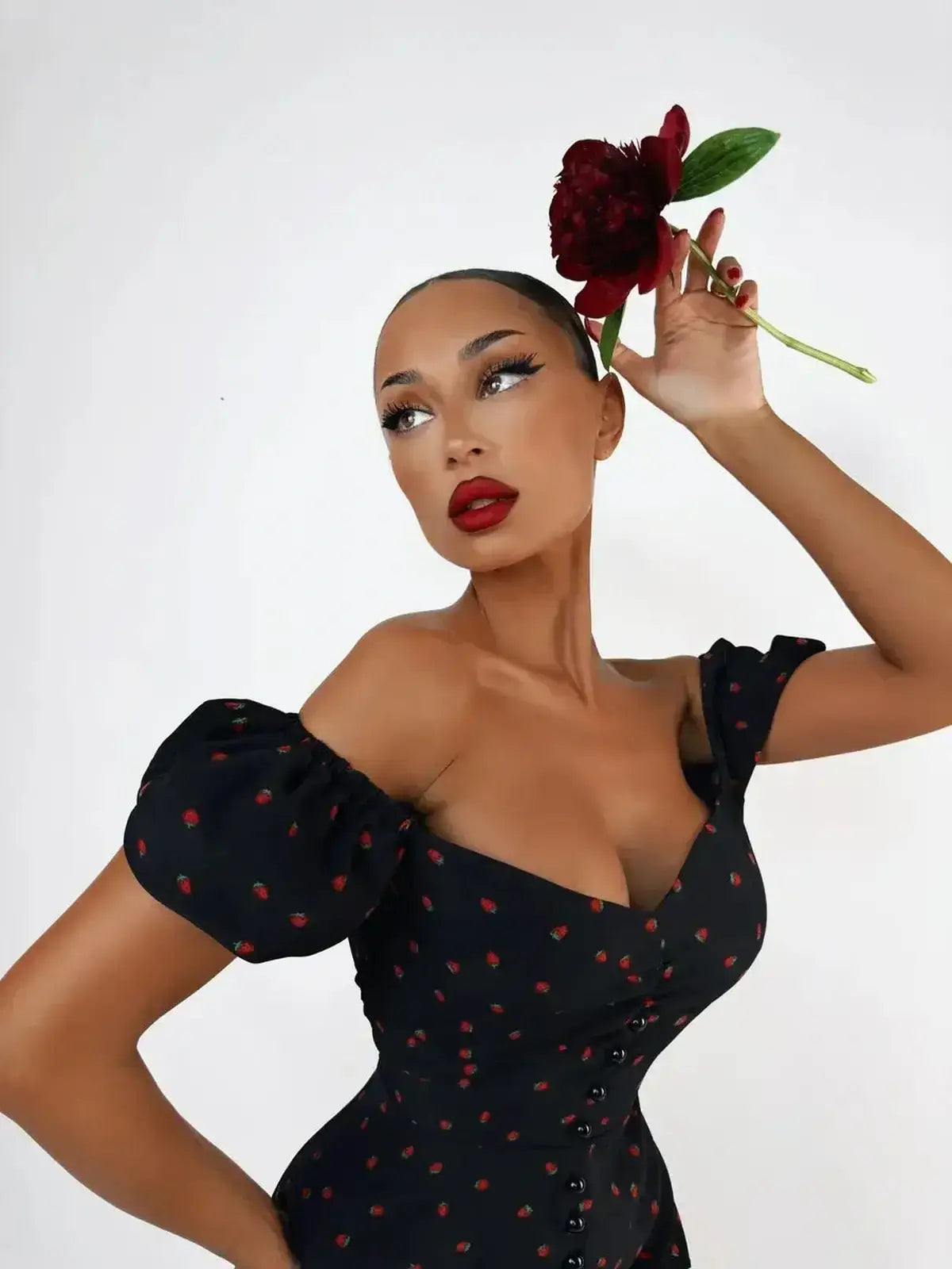 Model showcasing the Cherry Kiss Mini Dress with a cherry print, puff sleeves, and a flower accessory.