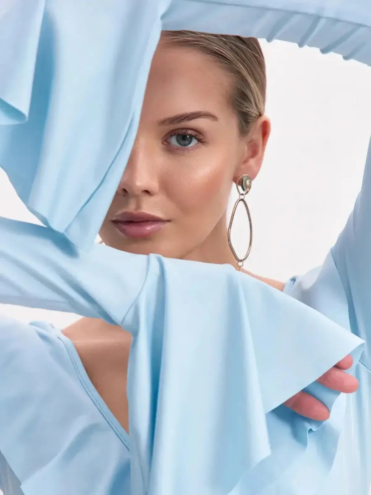 Close-up of a model wearing a light blue long sleeve dress with ruffled sleeves and elegant earrings.