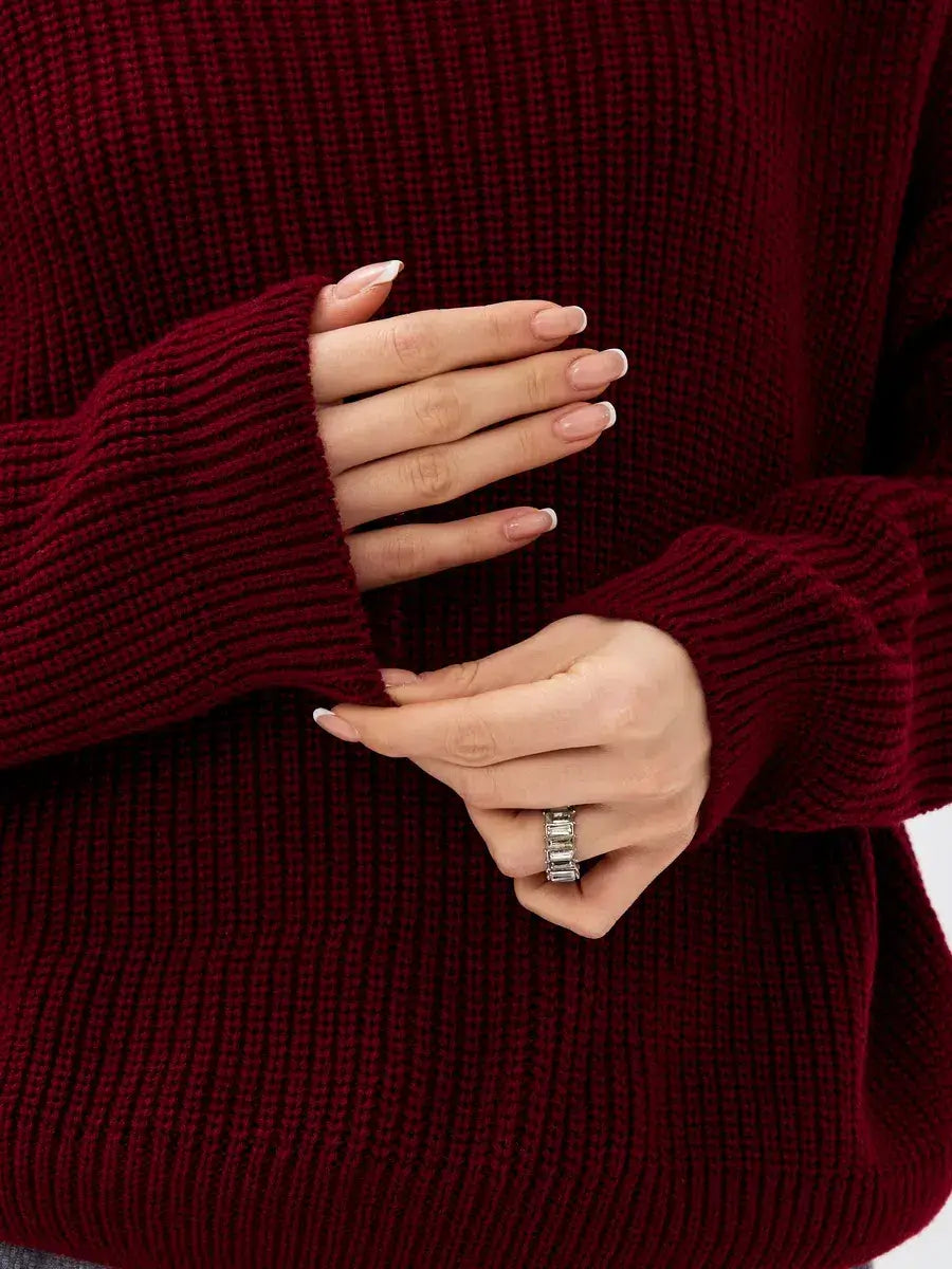 Close-up of hands wearing a ring while adjusting the sleeves of the Crimson Pullover by Lauven in burgundy.
