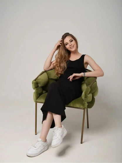 Model showcasing the Eclipse Maxi Dress, a sleek black dress styled with white sneakers, seated in a green chair.
