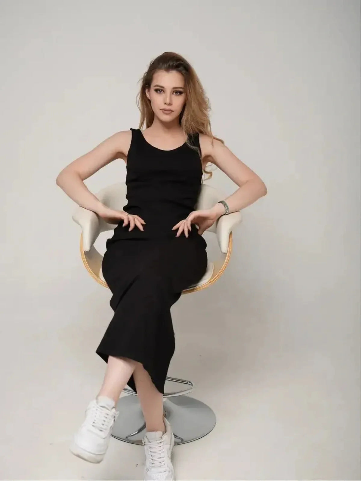 Model showcasing the Eclipse Maxi Dress, a sleek black sleeveless dress, styled with white sneakers.