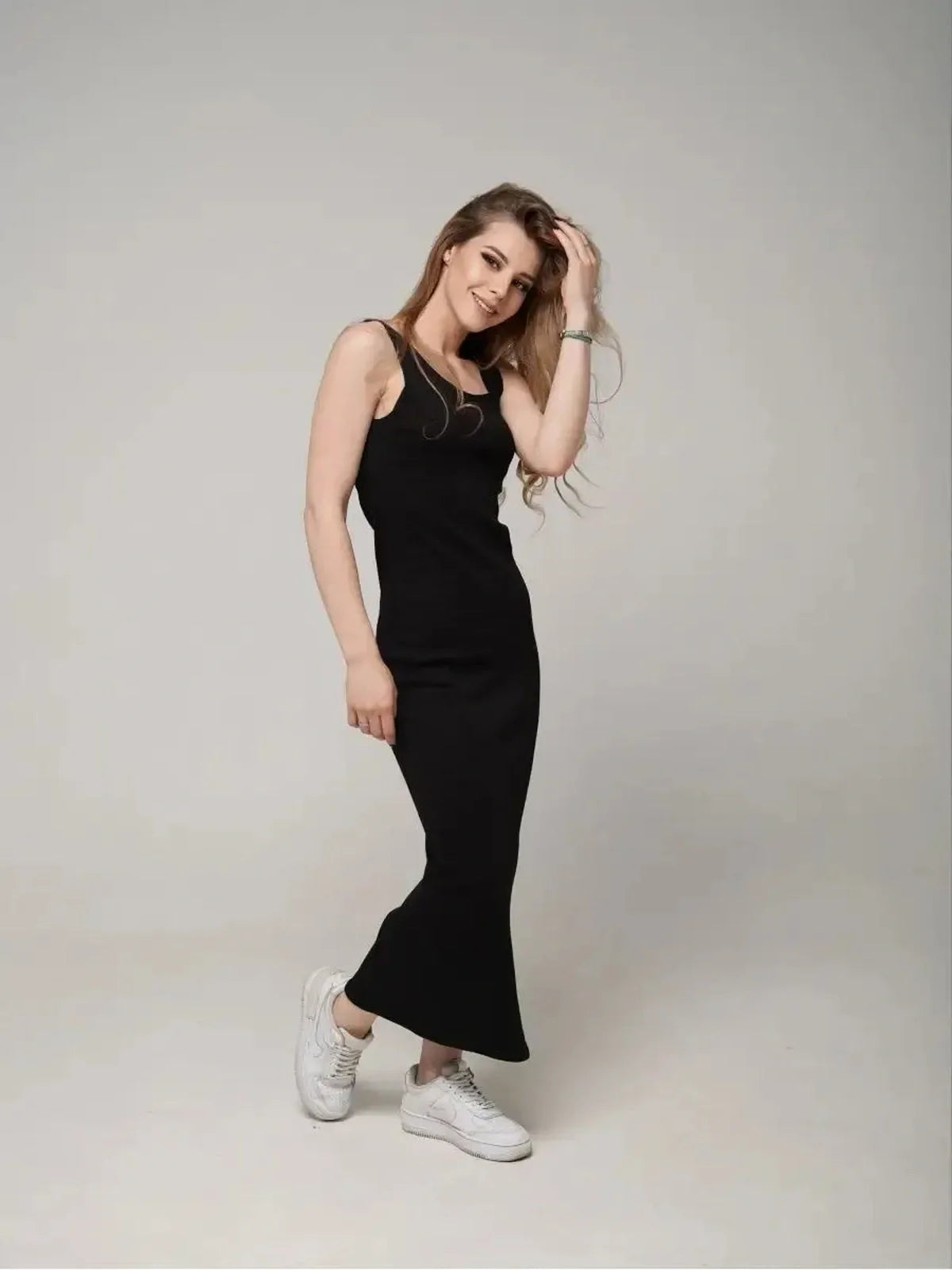 Model wearing the Eclipse Maxi Dress, a sleek black sleeveless dress paired with white sneakers, showcasing effortless elegance.