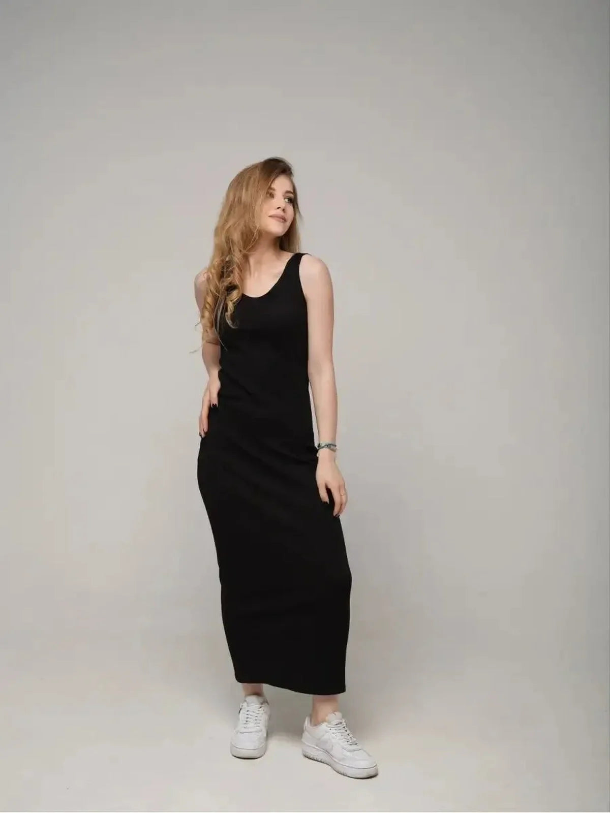 Model wearing the Eclipse Maxi Dress, a sleek black sleeveless dress, styled with white sneakers for a chic look.