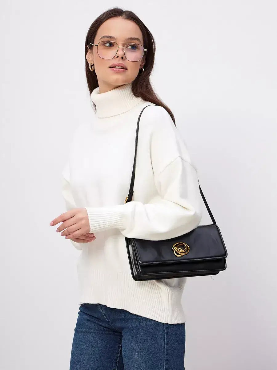 Model wearing the Elara Sweater by Lauven, a milk white turtleneck knitwear, paired with a black handbag.