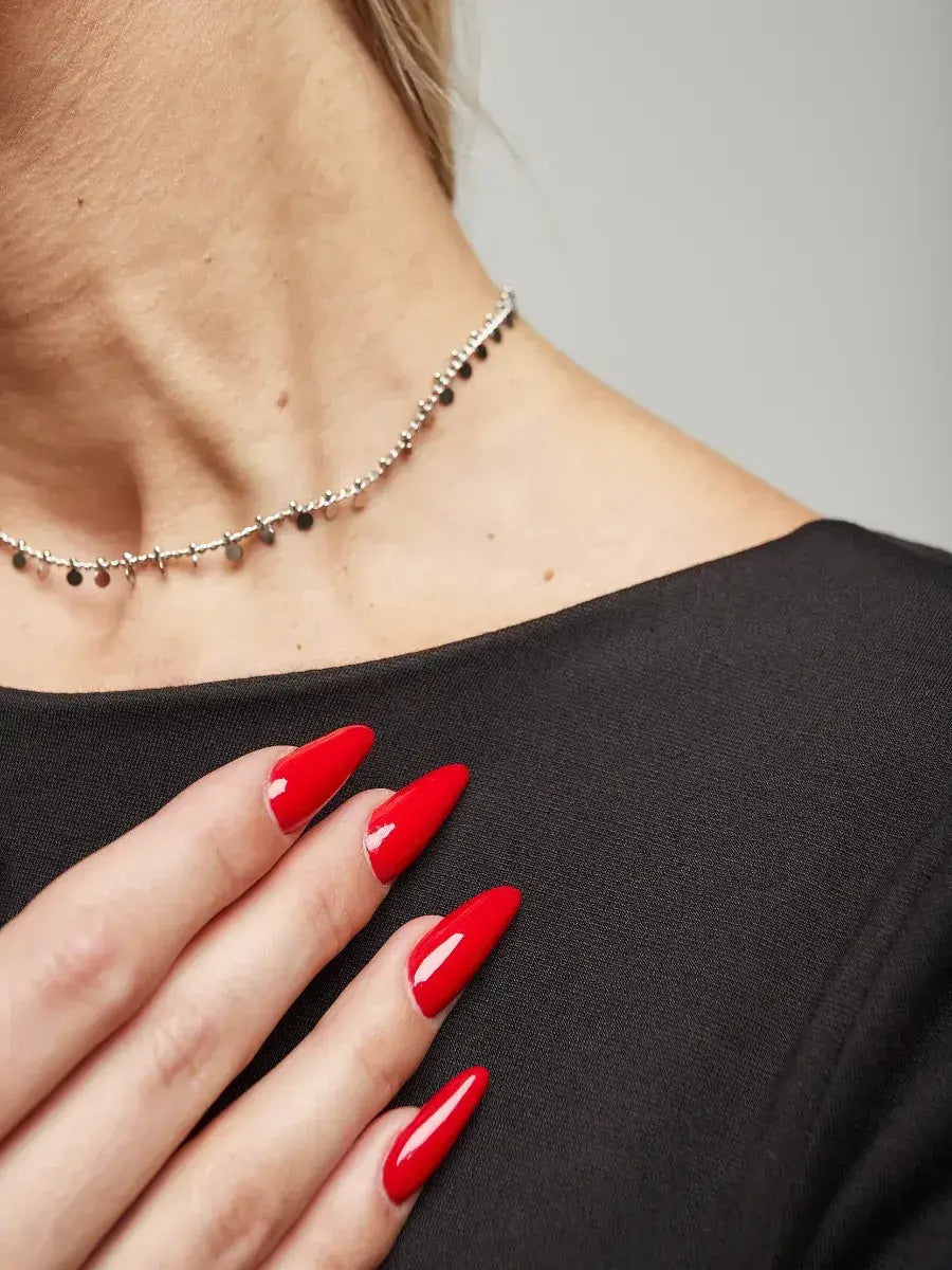 Close-up of a woman wearing a silver necklace and vibrant red nails, showcasing elegance for stylish occasions.