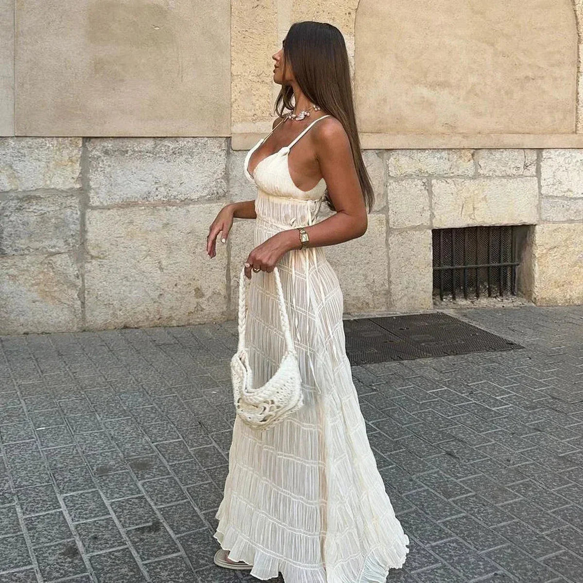 Side view of a woman in a white maxi dress with delicate shirring and a crochet bag, perfect for summer occasions.