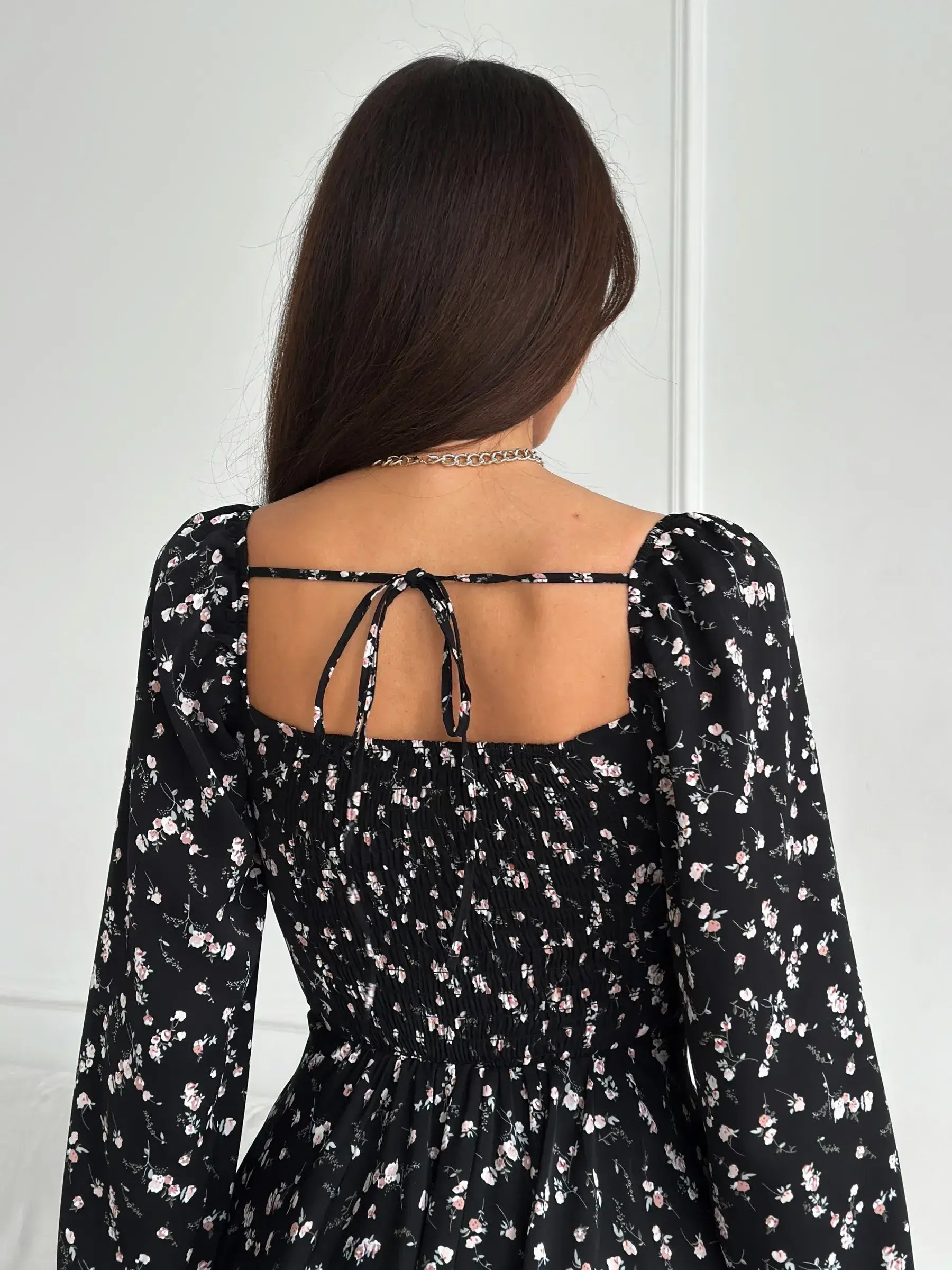 Back view of a woman in a floral black mini dress with long sleeves, showcasing its stylish design.