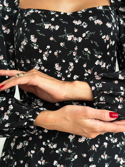 Close-up of hands in a floral black mini dress, showcasing romantic style and elegant long sleeves for women.