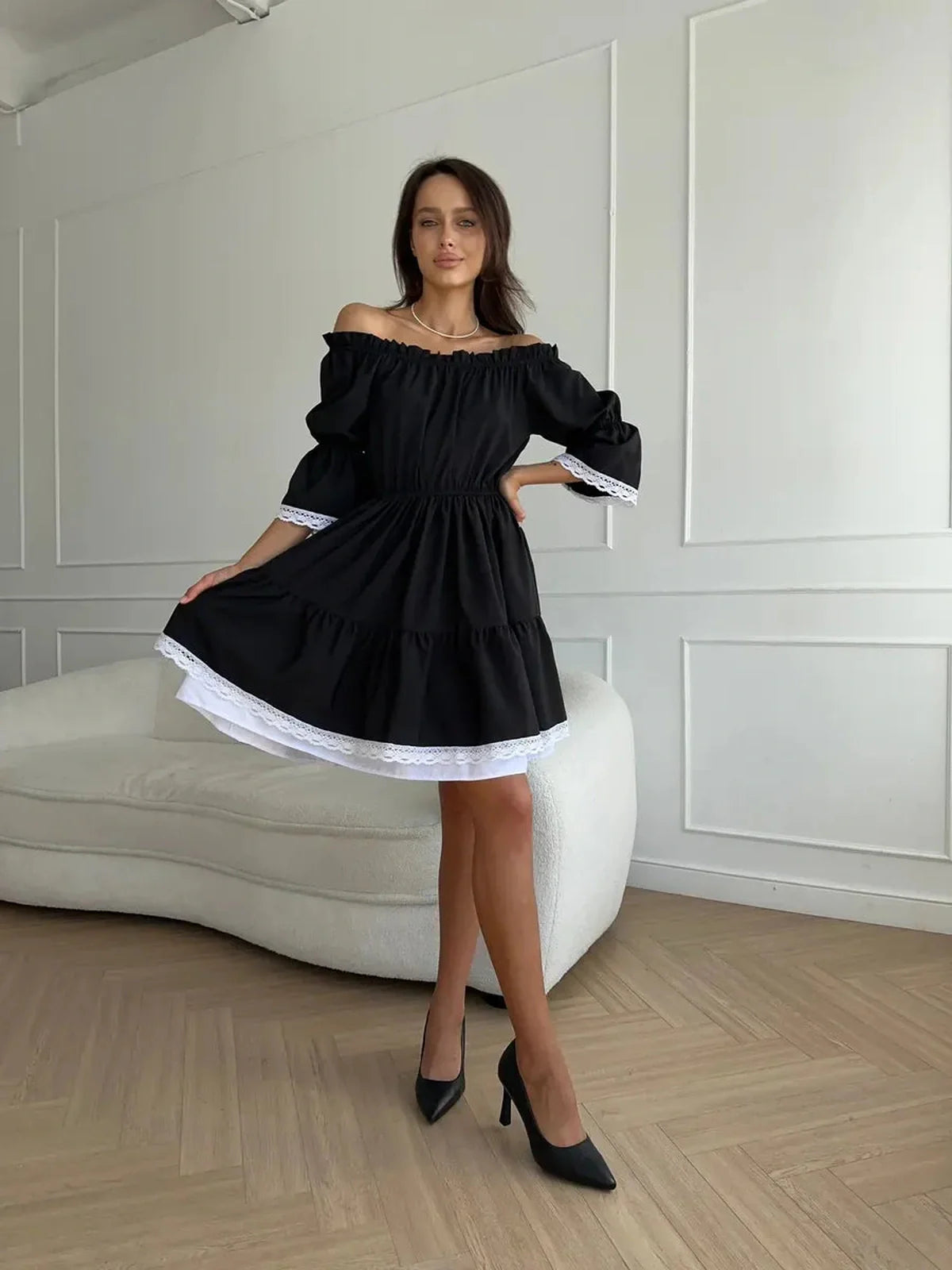 Model showcasing the Contrast Charm black mini dress with off-shoulder neckline and white lace trim.