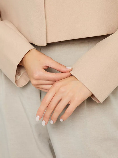 Close-up of hands adjusting the sleeve of the Sahara Blazer, a chic women’s beige cropped jacket by Lauven.