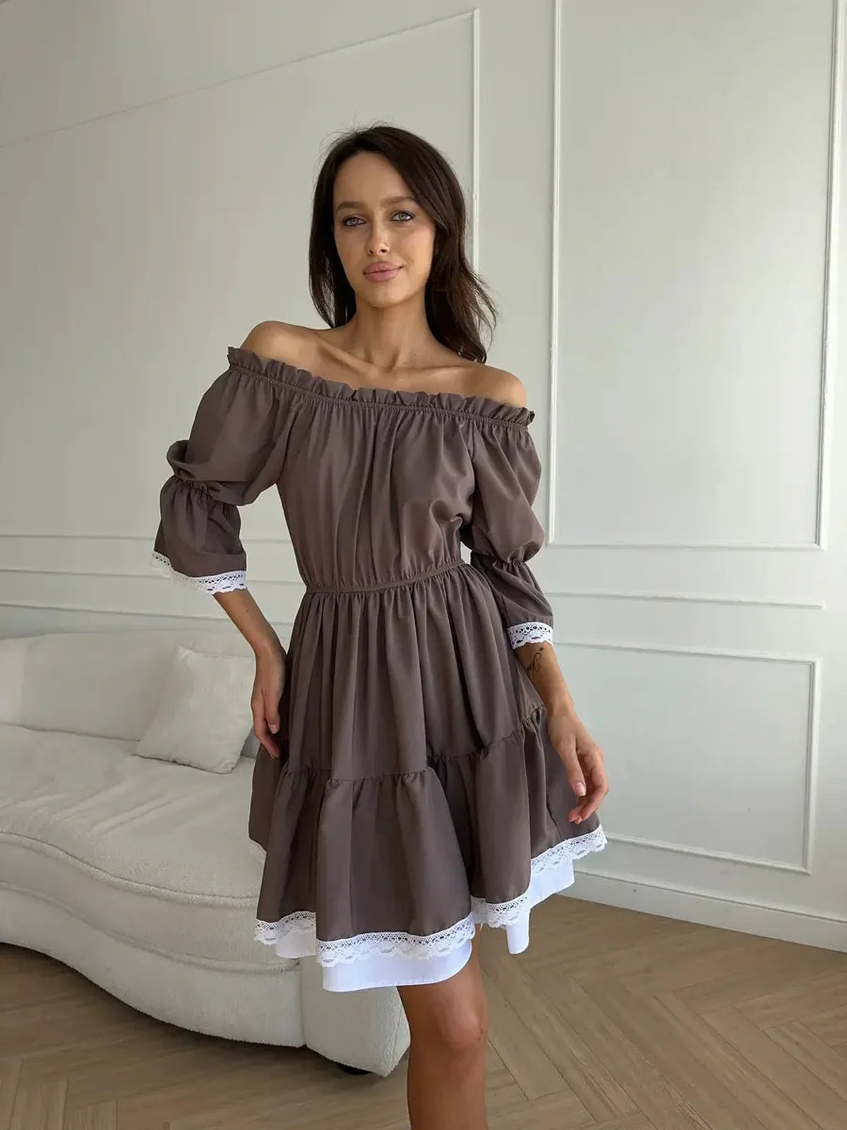Off-shoulder mocha mini dress with ruffle trim, perfect for summer styled in a chic indoor setting.