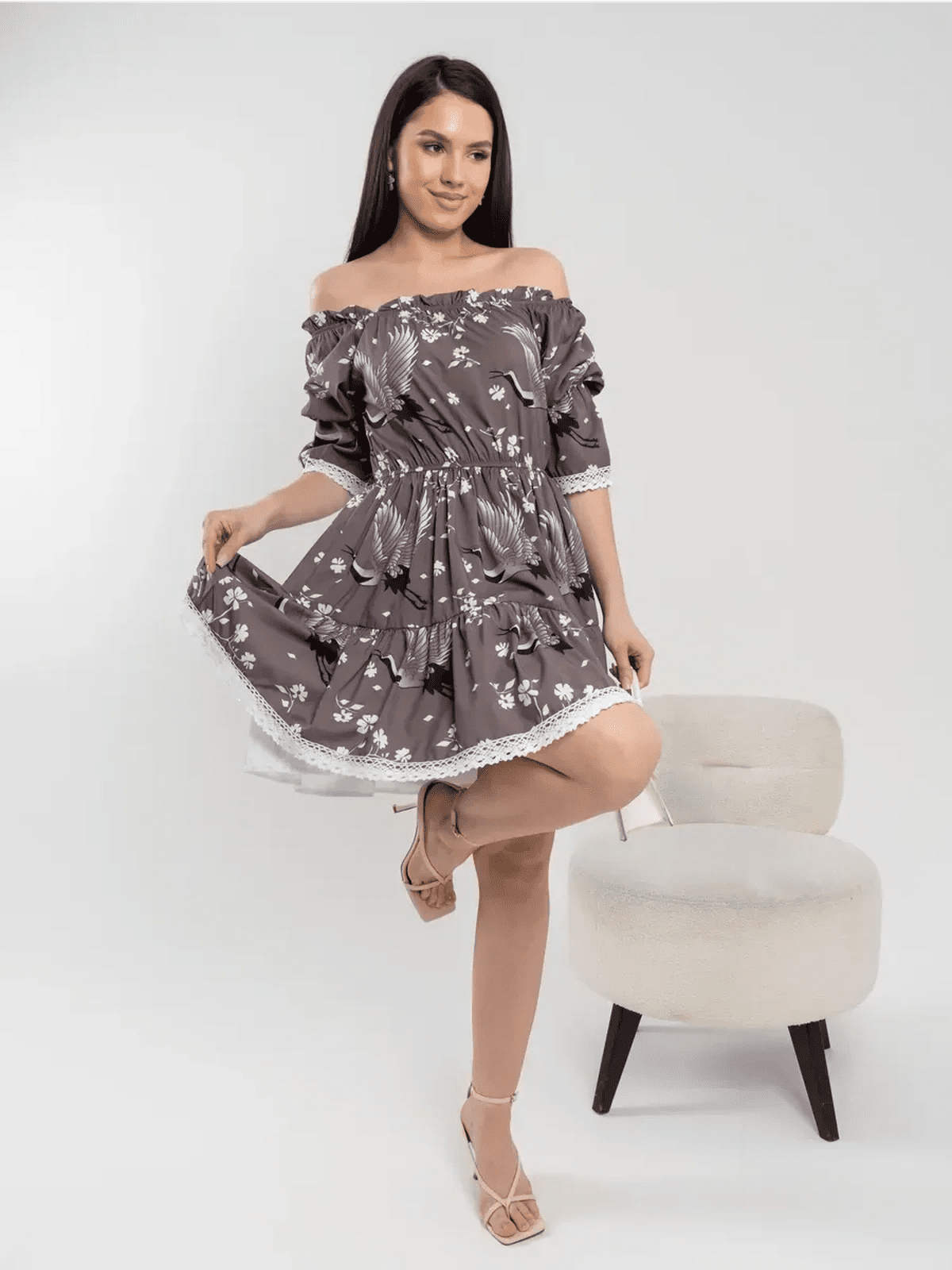 Model wearing the Sakura Flight off-shoulder mini dress with cranes and cherry blossoms in grey-brown fabric.