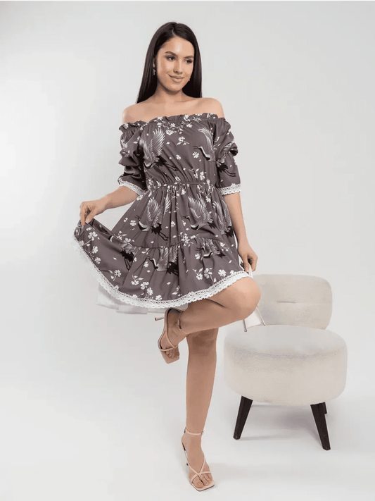 Model wearing the Sakura Flight off-shoulder mini dress with cranes and cherry blossoms in grey-brown fabric.