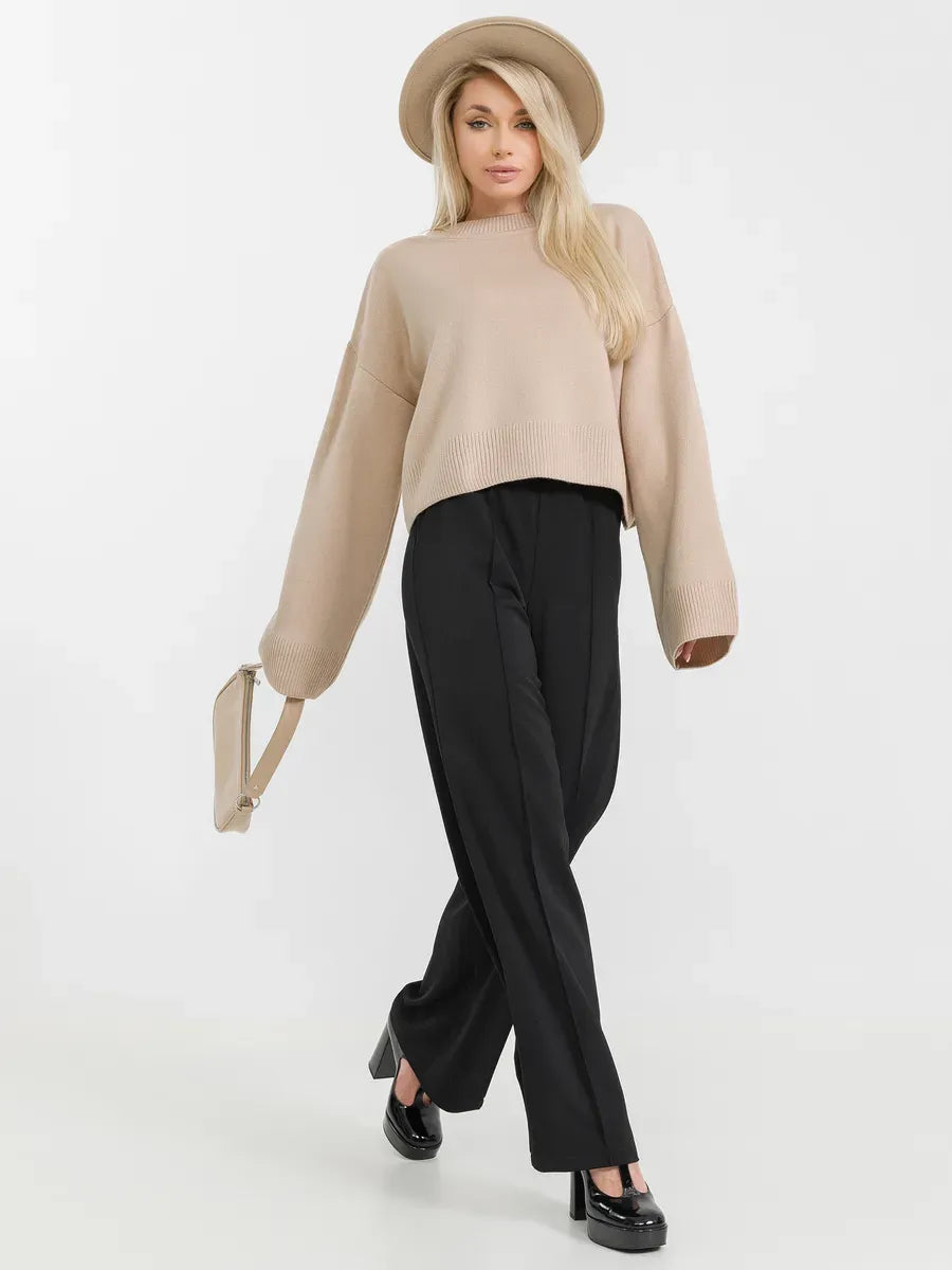 Woman wearing a beige knit Siena Sweater with black pants and a hat, showcasing effortless sophistication by Lauven.
