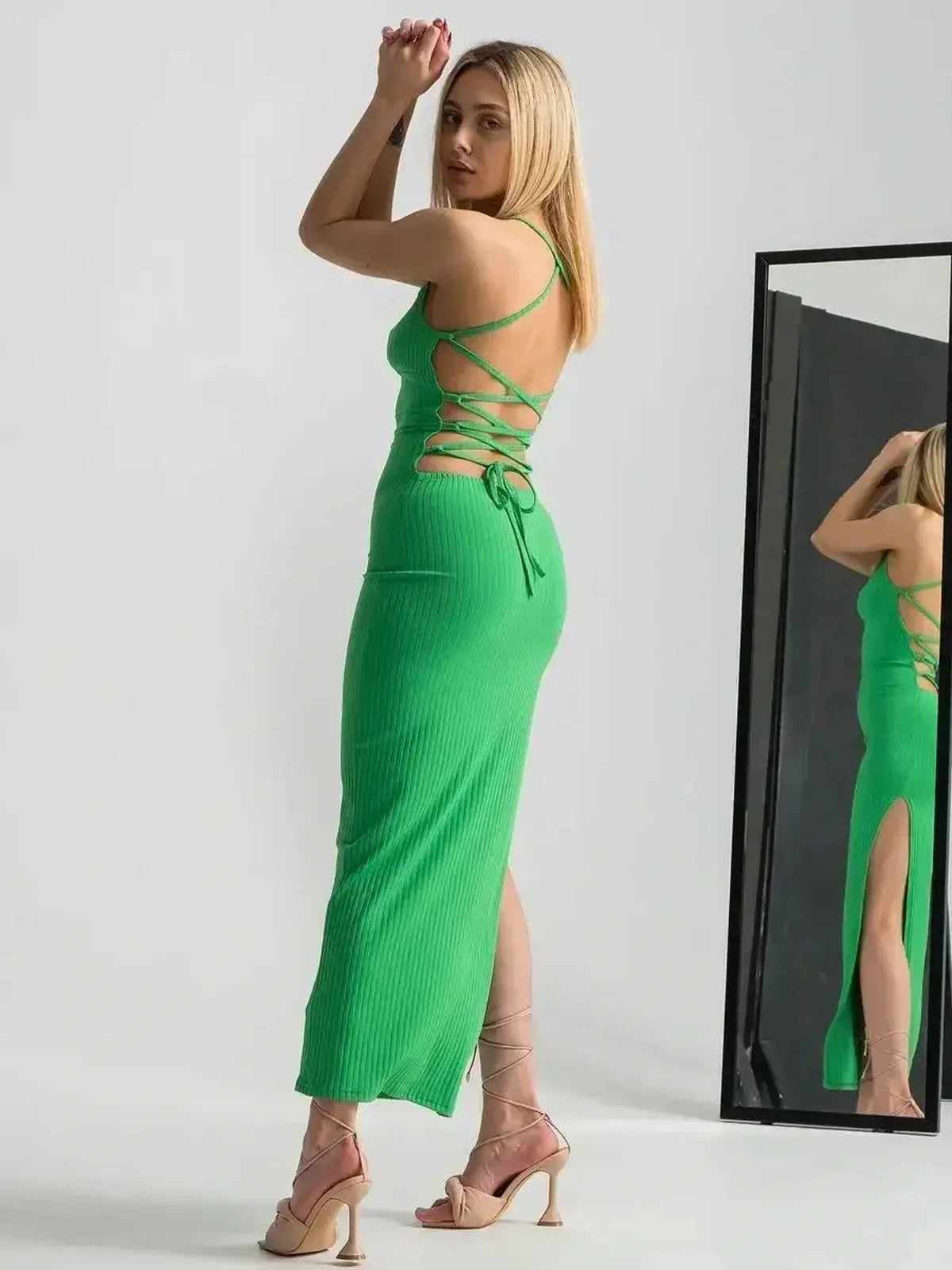 Model in a sleeveless green maxi dress with strappy back and dramatic leg slit, showcasing elegance and style.