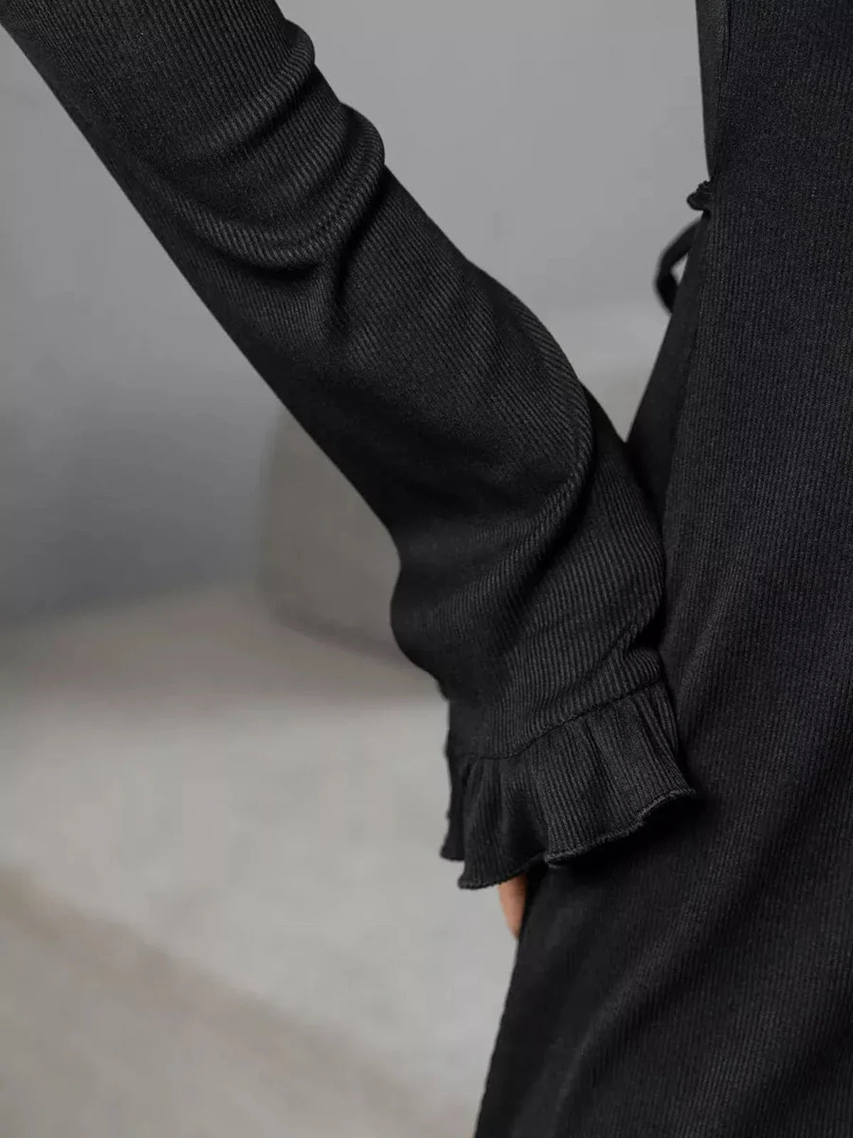 Close-up of the Noir Flare dress showcasing its long sleeve and elegant ruffled trim in a sleek black fabric.