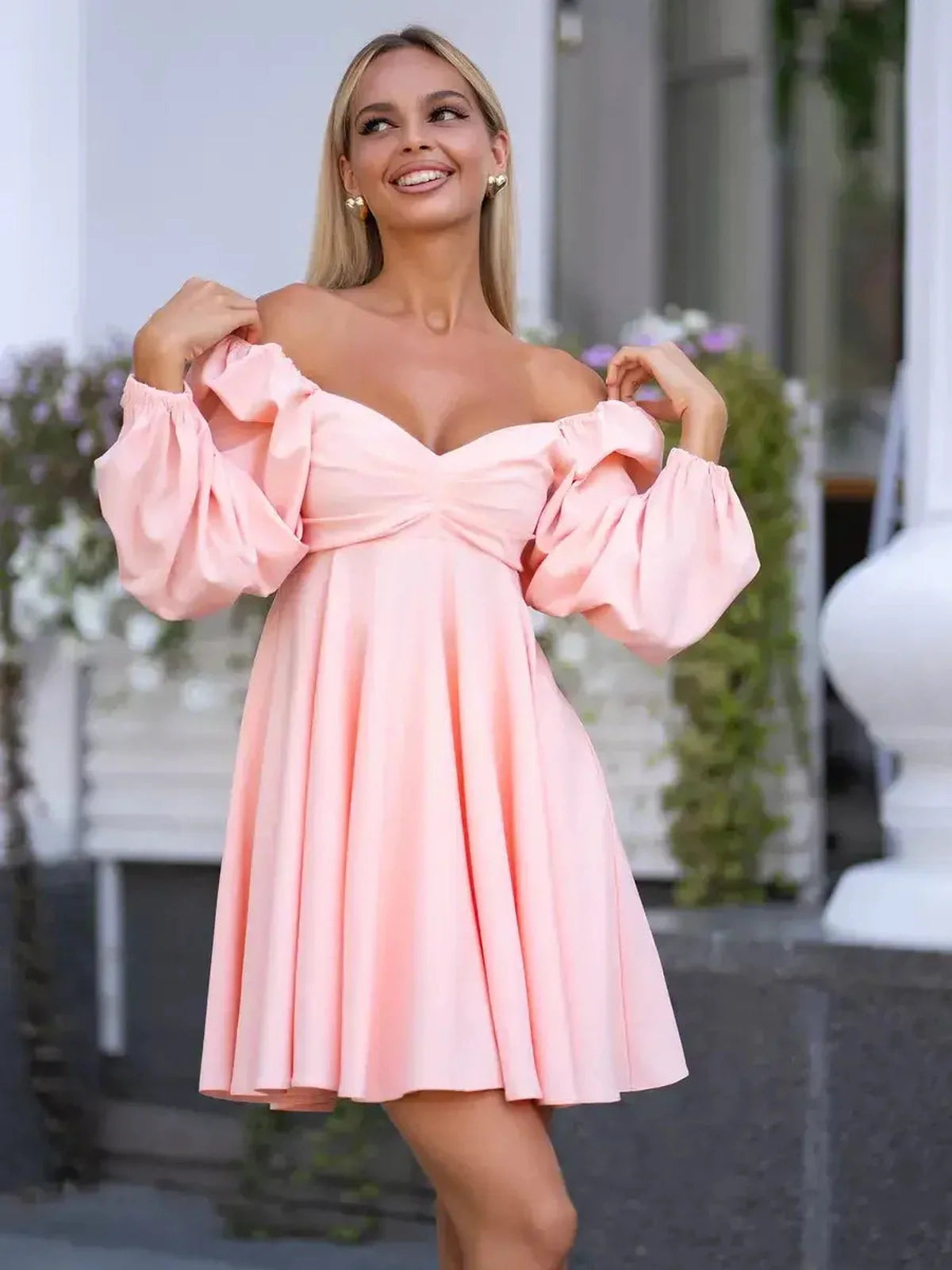 Model wearing a peach-pink mini dress with voluminous sleeves and a flattering neckline, perfect for summer occasions.