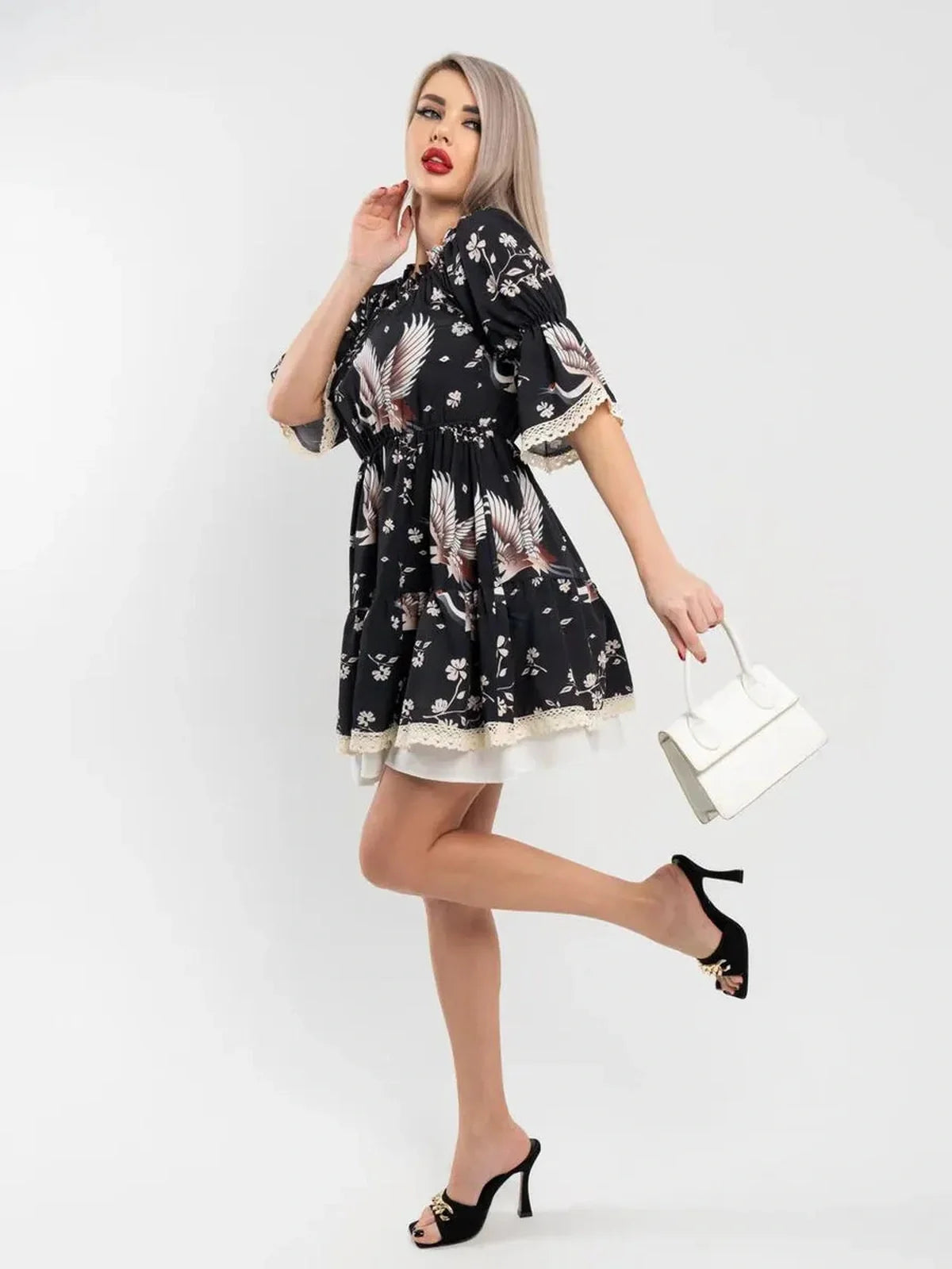 Model poses in off-shoulder Crane Bloom mini dress with crane and floral print, emphasizing elegance and vintage style.