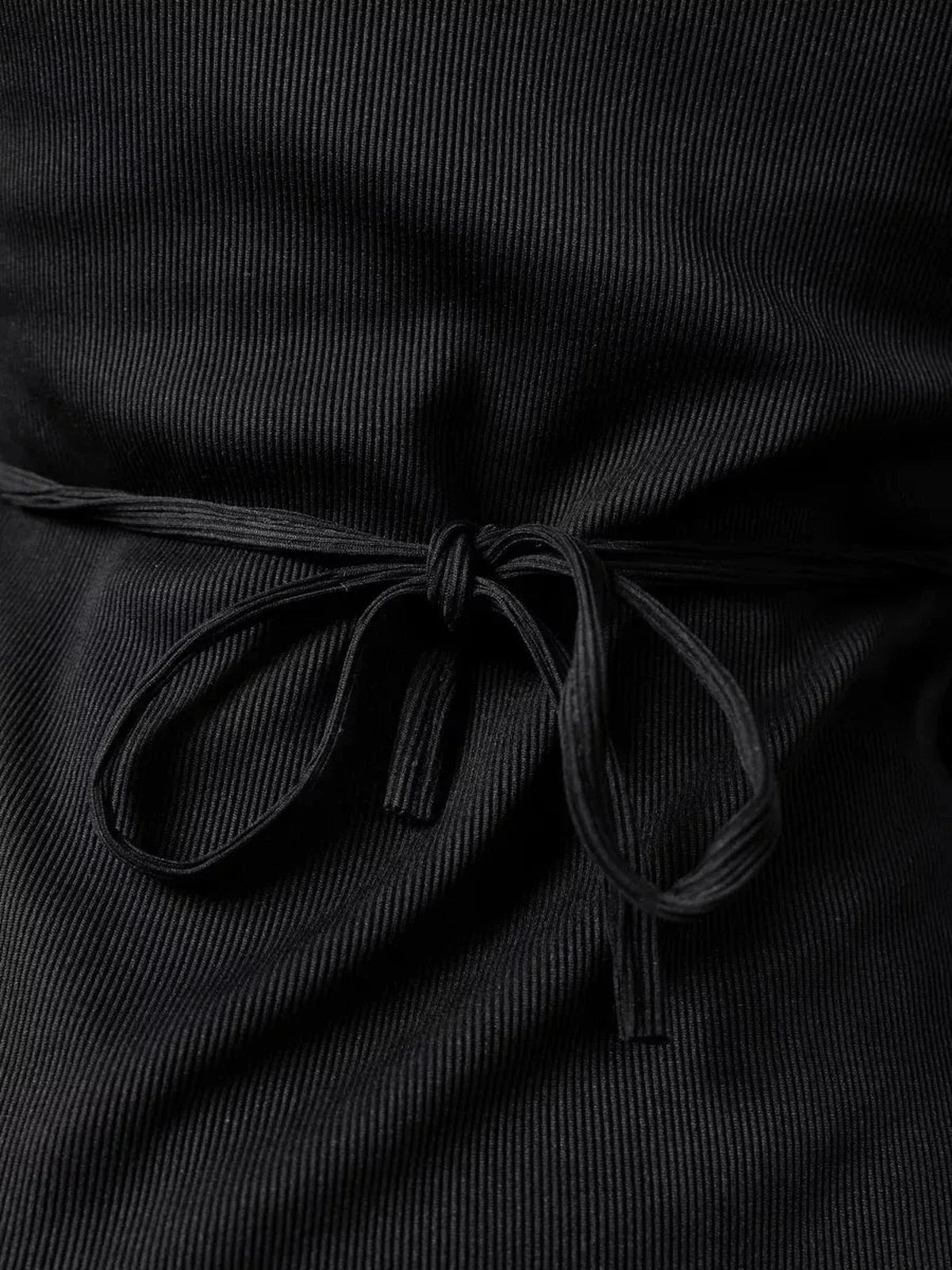 Close-up of lace-up back detail of Noir Flare mini dress, showcasing black ribbed fabric and stylish bow.