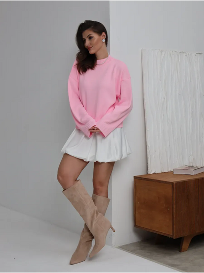 Model showcasing the Lyra Sweater in soft pink by Lauven, paired with a white skirt and knee-high boots.