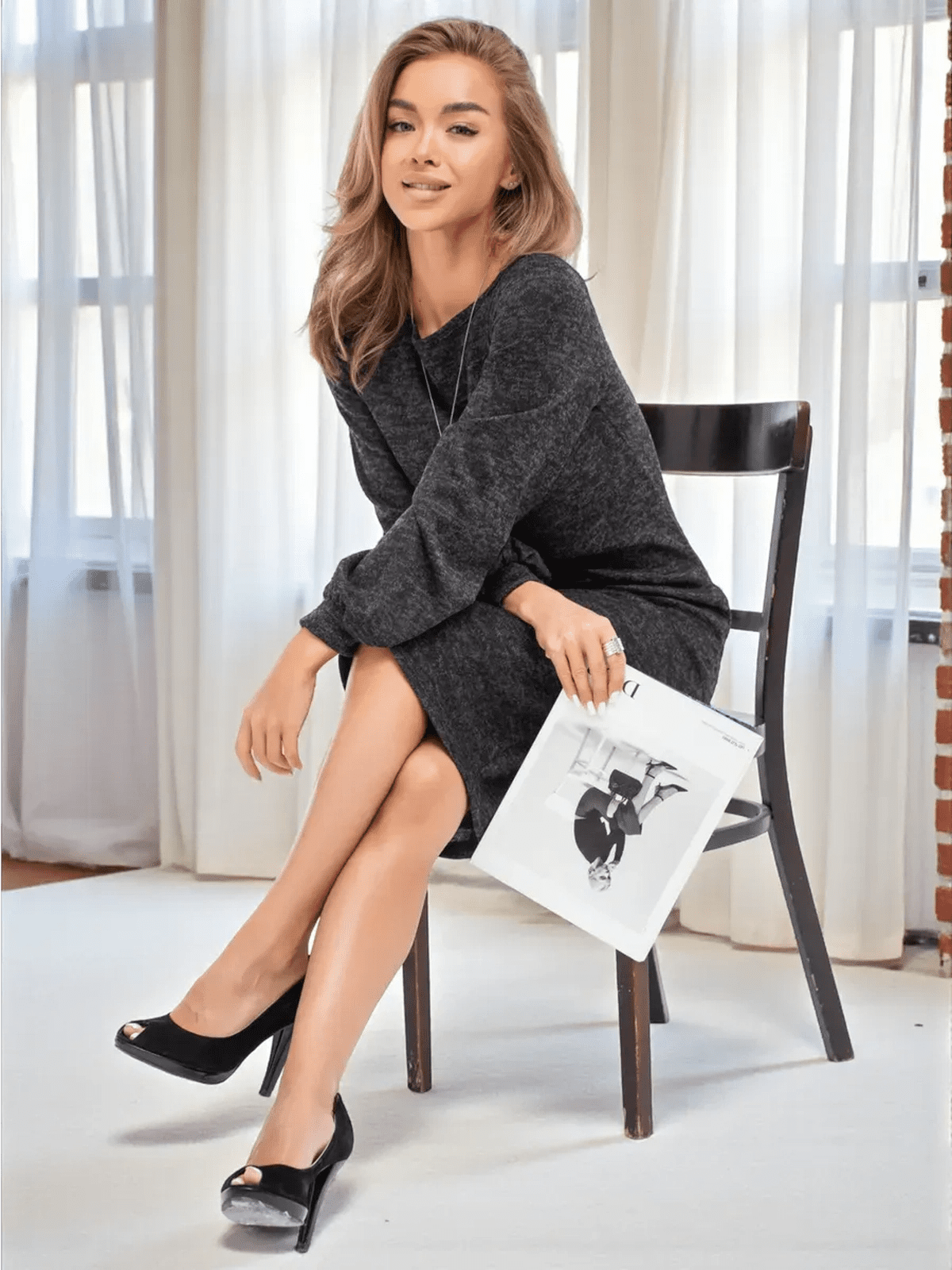 Woman in a graphite-black Noir Midi Dress by Lauven, exuding elegance while sitting with a magazine.
