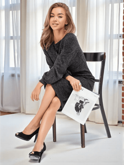 Woman in a graphite-black Noir Midi Dress by Lauven, exuding elegance while sitting with a magazine.