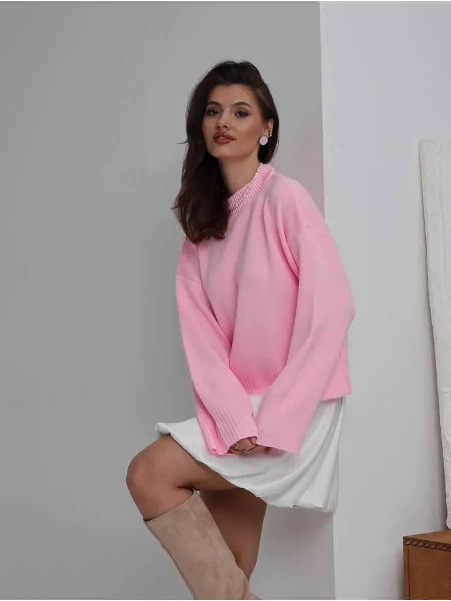 Model wearing the Lyra Sweater by Lauven, an oversized knit in soft pink, paired with a chic white outfit.
