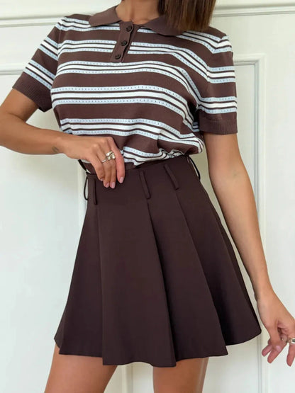 Model wearing Verona Mini Skirt by Lauven, a chocolate brown pleated A-line skirt paired with a striped polo.