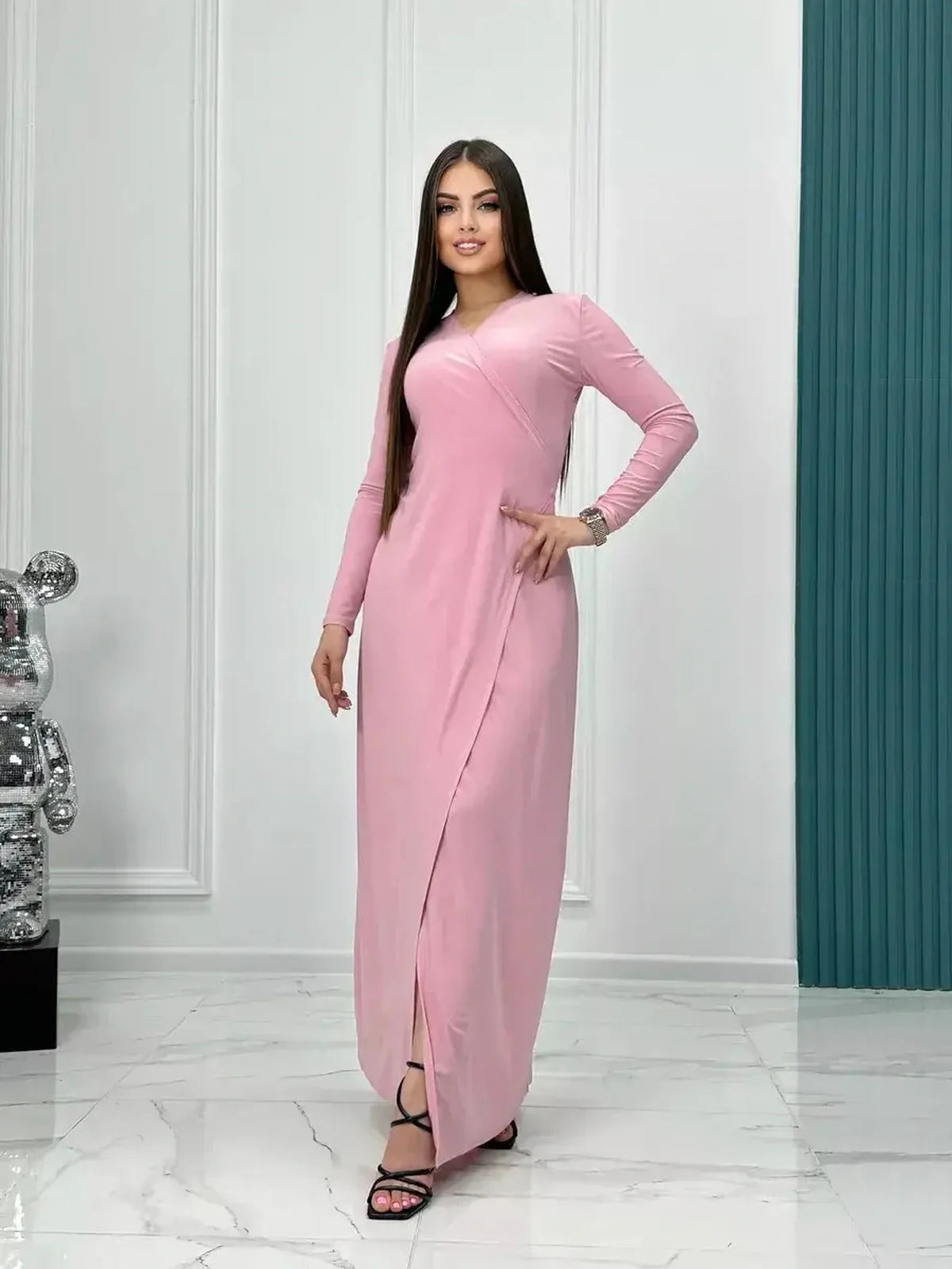 Model showcasing the Eclipse Maxi Dress in powder pink with long sleeves and a wrap silhouette, styled elegantly.