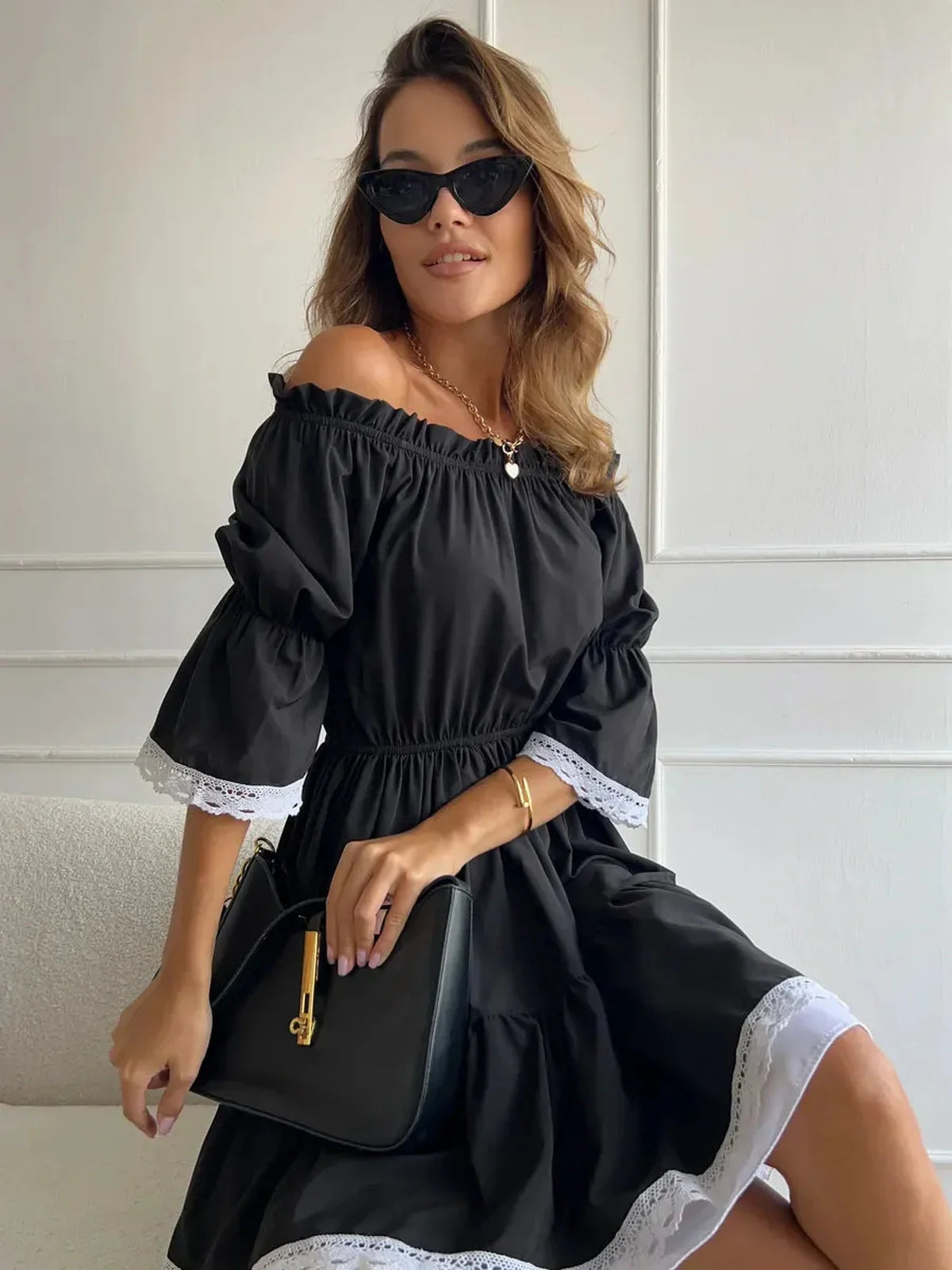 Model wearing a black off-shoulder mini dress with white lace trim, showcasing timeless elegance and romantic flair.