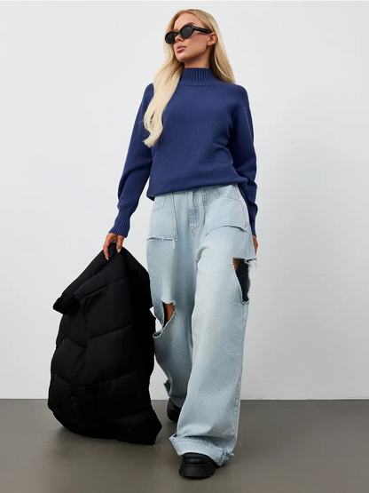 Indigo Sweater by Lauven showcased in an oversized navy blue cashmere knit with high neck, paired with light denim and a puffer jacket.