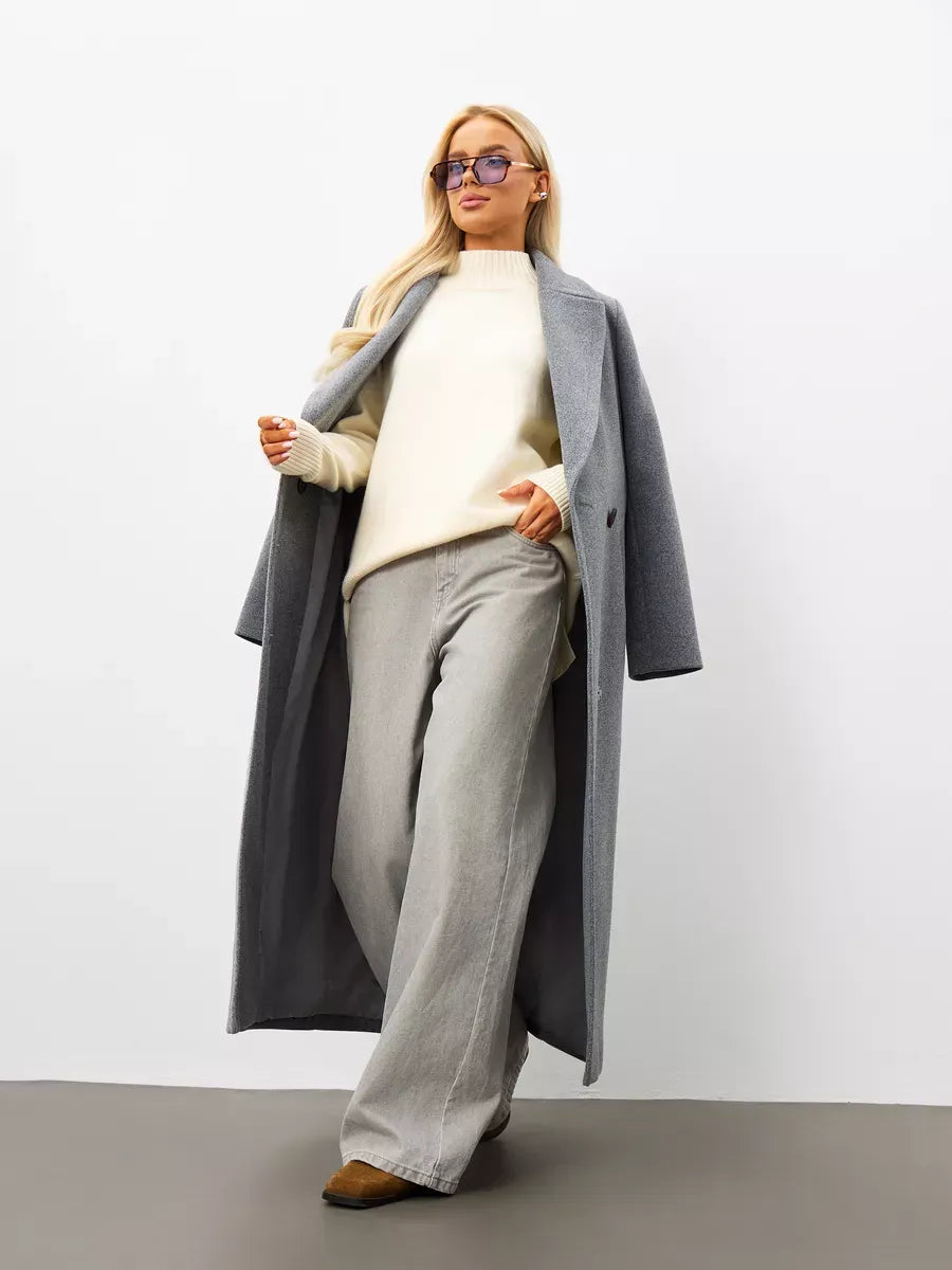 Model showcasing the Liora Sweater, an oversized cashmere knitwear, paired with a long grey coat and wide-leg pants.