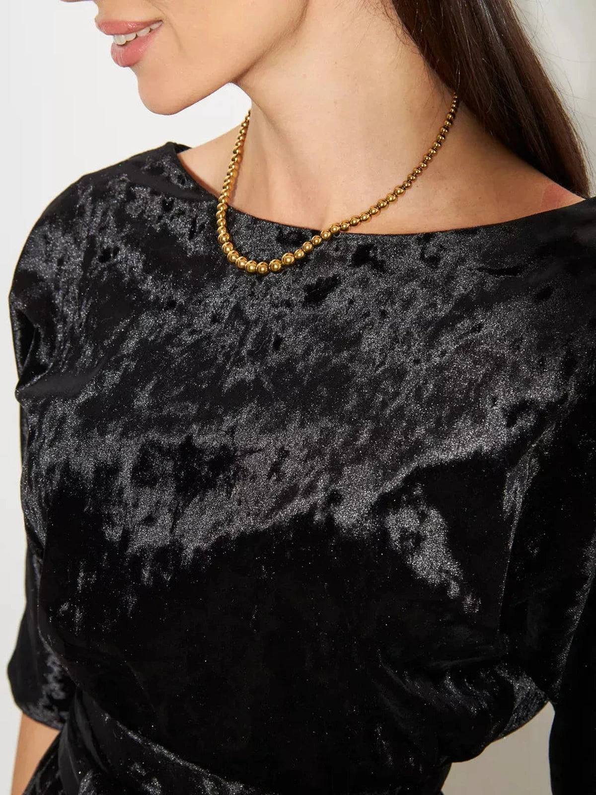 Close-up of a woman wearing the Noiré Maxi Dress by Lauven, showcasing black velvet texture and gold necklace.