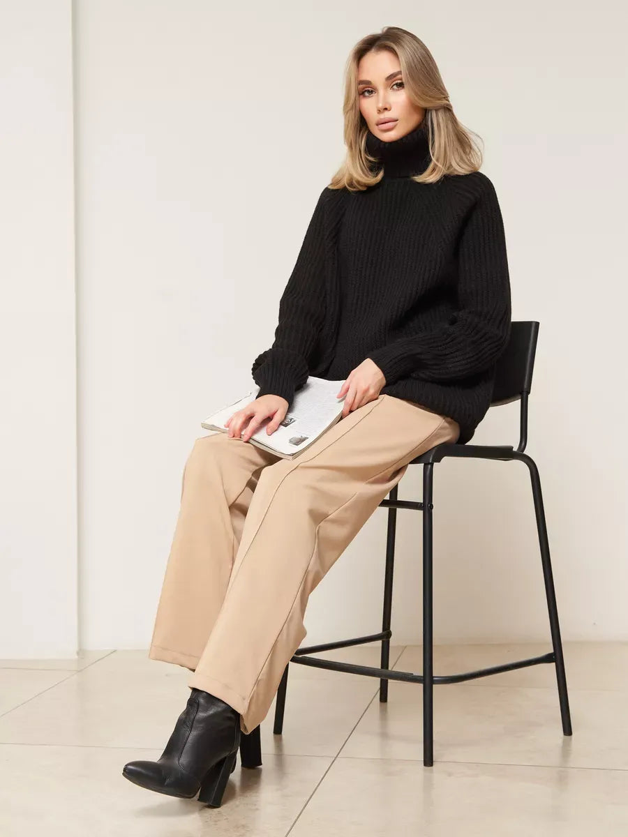Model wearing the Onyx Sweater by Lauven, an oversized black knitwear with turtleneck, styled with beige pants.