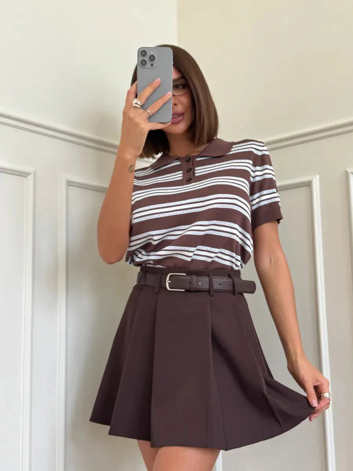 Model wearing Verona Mini Skirt by Lauven, a chocolate brown pleated A-line skirt with a stylish striped top.