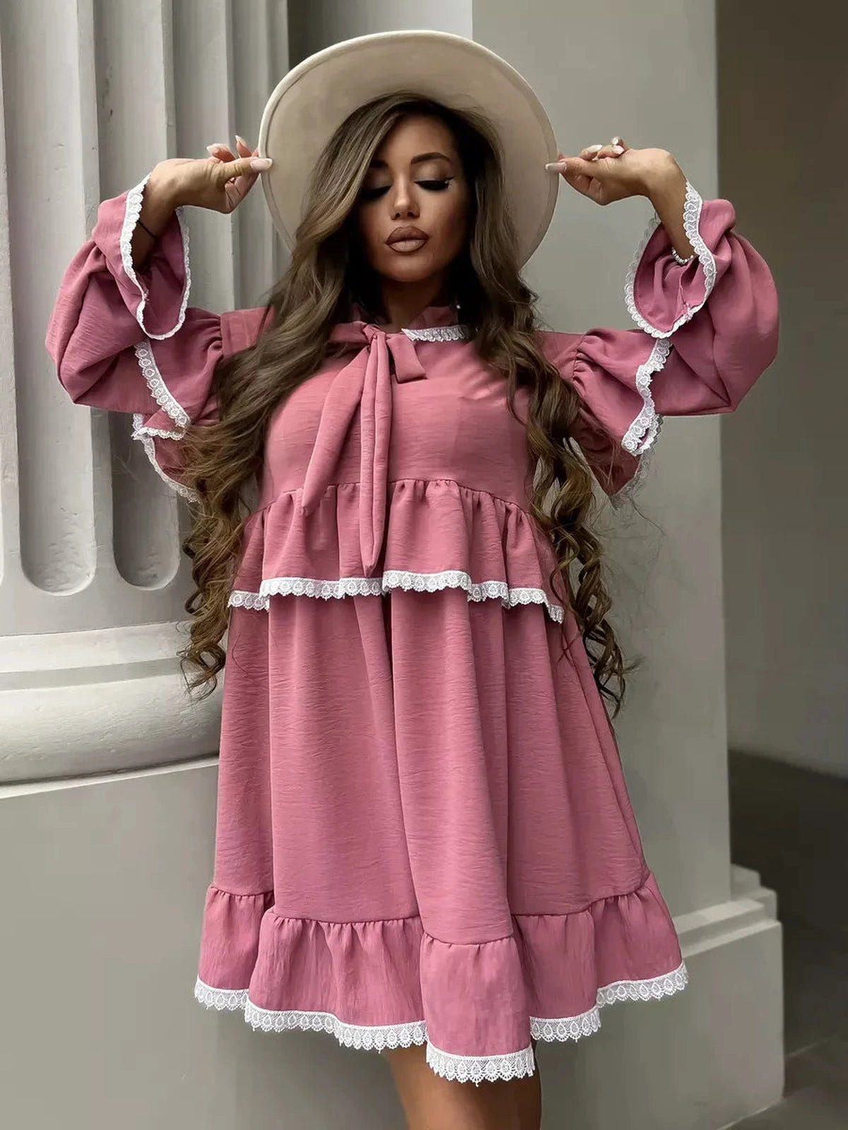 Model wearing a pink Rosea Mini Dress by Lauven, featuring ruffles and lace details, styled with a wide-brim hat.