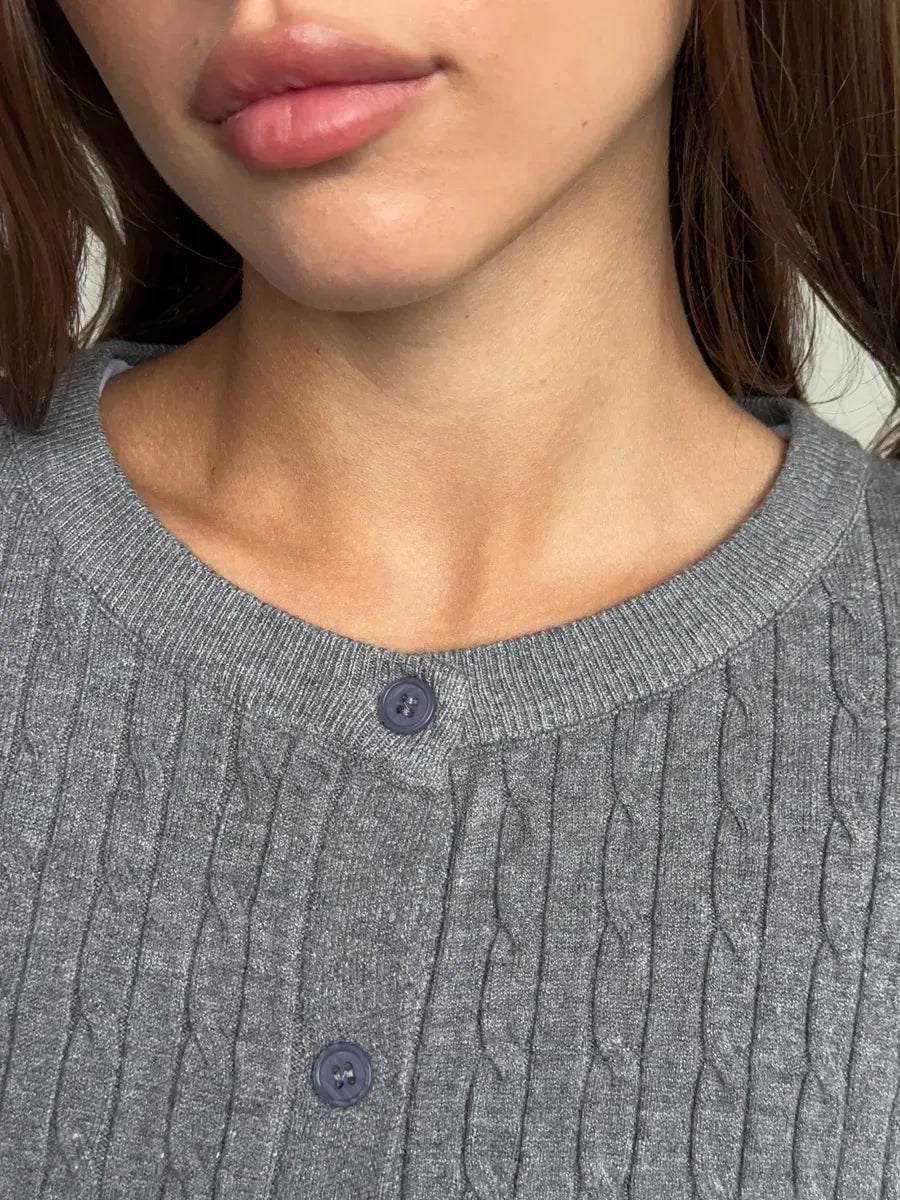 Close-up of a woman wearing the Sterling Cardigan by Lauven, showcasing the grey cable knit detail and button closure.